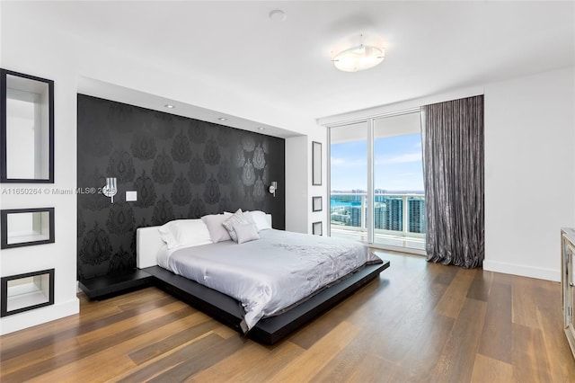 bedroom with access to outside, dark hardwood / wood-style flooring, and a wall of windows