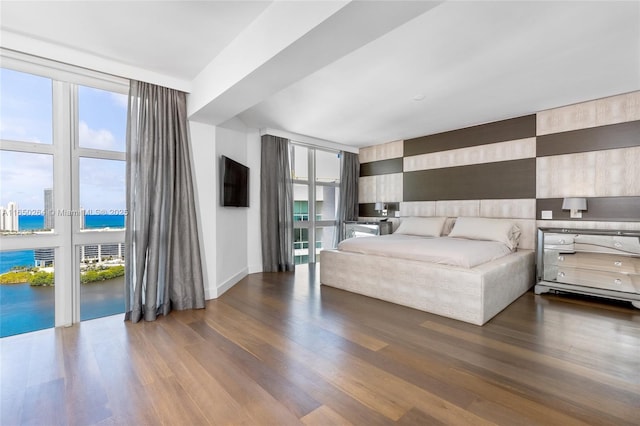 bedroom featuring wood-type flooring, a water view, and a wall of windows