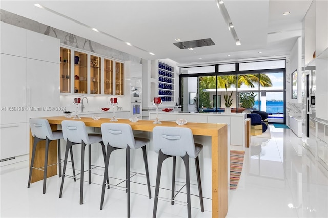 kitchen featuring butcher block counters, white cabinetry, white double oven, a breakfast bar area, and light tile patterned floors