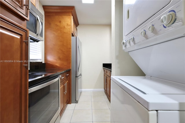 kitchen with stainless steel appliances, light tile patterned flooring, and stacked washing maching and dryer