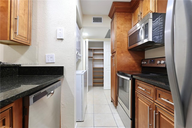 kitchen with visible vents, dark stone counters, light tile patterned floors, appliances with stainless steel finishes, and brown cabinetry