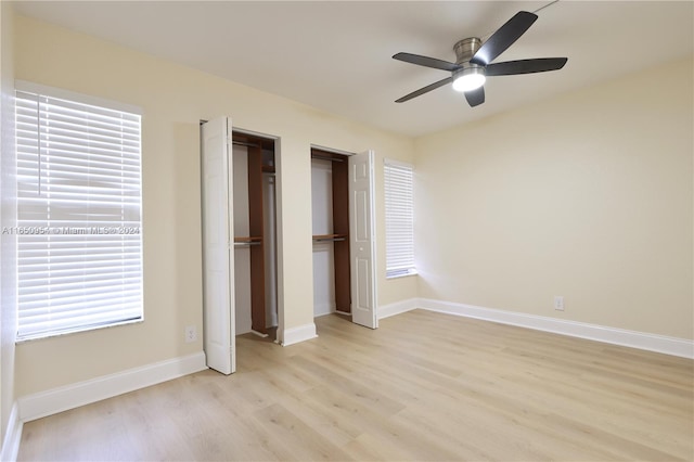 unfurnished bedroom with light wood-type flooring, baseboards, ceiling fan, and multiple closets