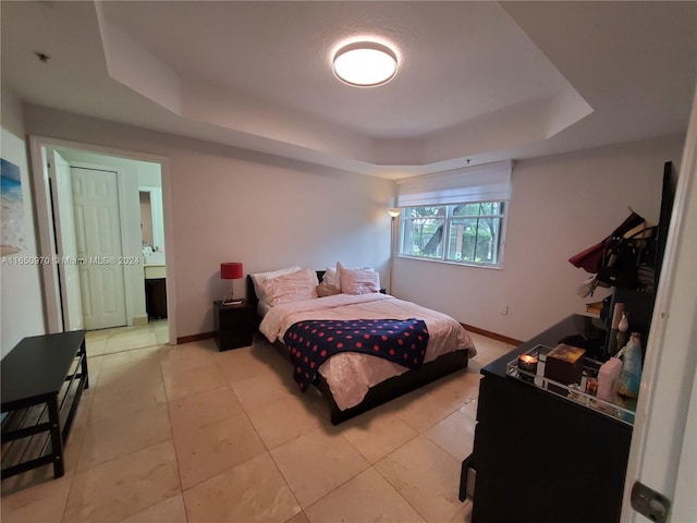 tiled bedroom featuring ensuite bath and a tray ceiling