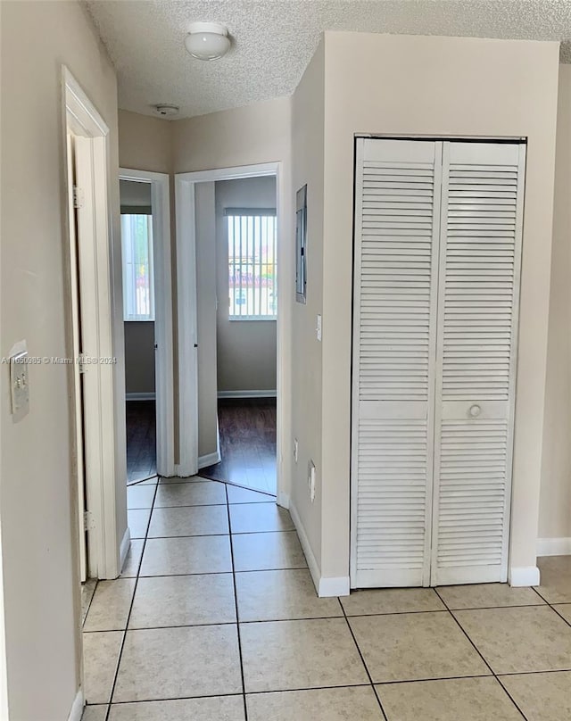 hallway with light tile patterned floors, baseboards, and a textured ceiling