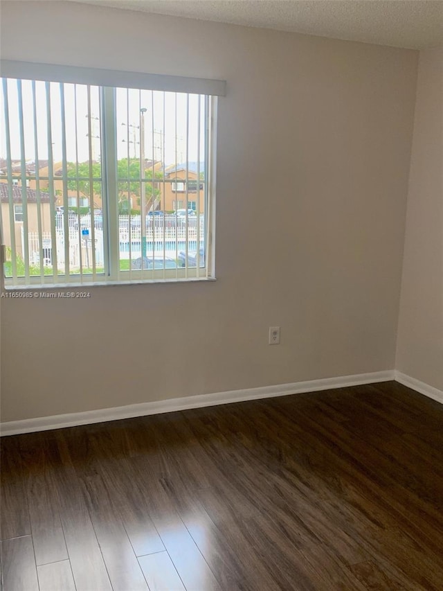 empty room featuring a textured ceiling, dark wood-type flooring, and baseboards