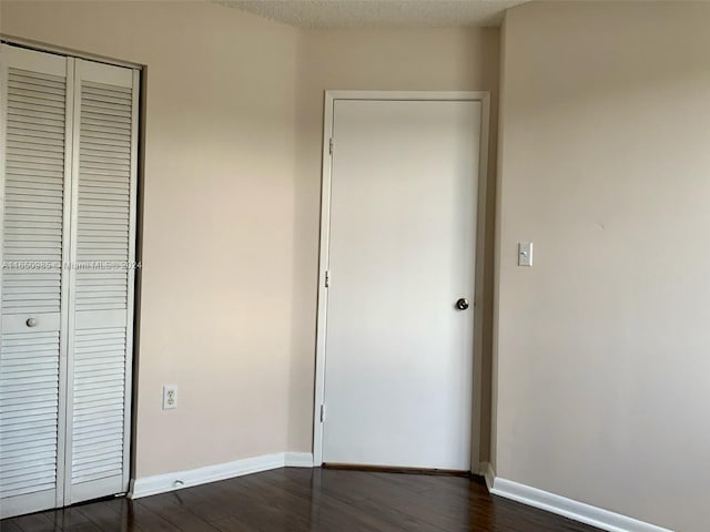 unfurnished bedroom with dark wood finished floors, a textured ceiling, a closet, and baseboards