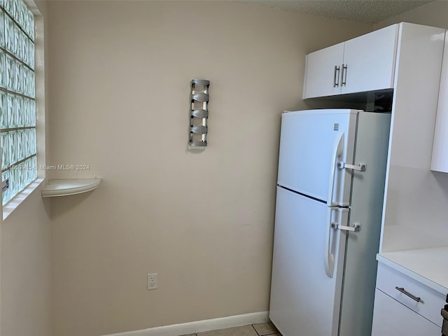 kitchen featuring white cabinetry, freestanding refrigerator, light countertops, light tile patterned floors, and baseboards