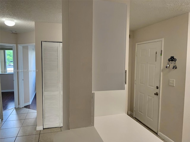 hallway featuring light tile patterned floors, baseboards, and a textured ceiling