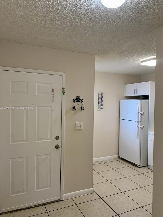 interior space featuring a textured ceiling, freestanding refrigerator, white cabinets, light tile patterned floors, and baseboards