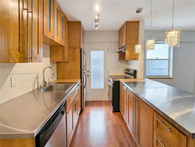 kitchen with light wood-type flooring, stainless steel appliances, stainless steel counters, sink, and hanging light fixtures