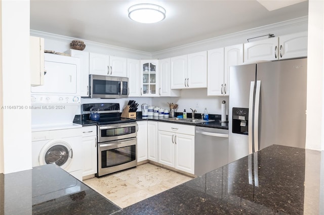 kitchen featuring dark stone countertops, appliances with stainless steel finishes, stacked washer / drying machine, and white cabinets