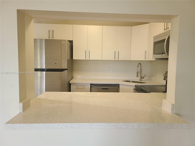 kitchen featuring white cabinets, light stone counters, stainless steel appliances, and sink