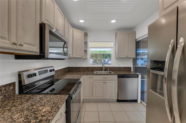 kitchen with sink, dark stone counters, stainless steel appliances, and light tile patterned floors