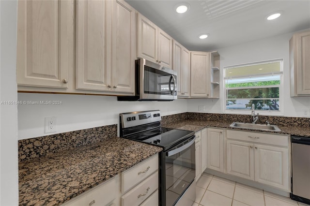 kitchen with appliances with stainless steel finishes, light tile patterned flooring, dark stone countertops, and sink