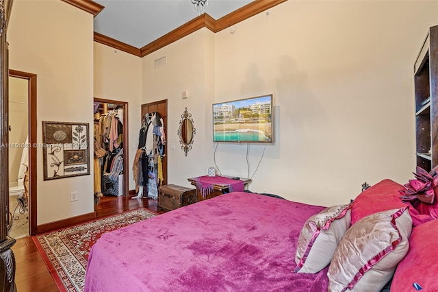 bedroom with a walk in closet, a closet, hardwood / wood-style floors, ornamental molding, and a high ceiling