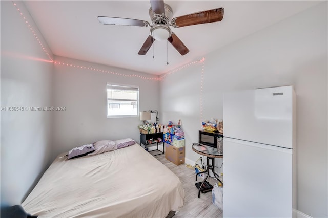 bedroom with light wood-type flooring, white refrigerator, and ceiling fan