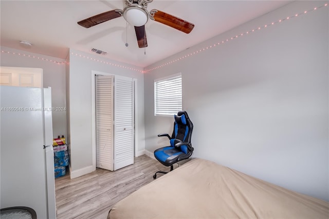 bedroom featuring white refrigerator, light hardwood / wood-style flooring, ceiling fan, and a closet