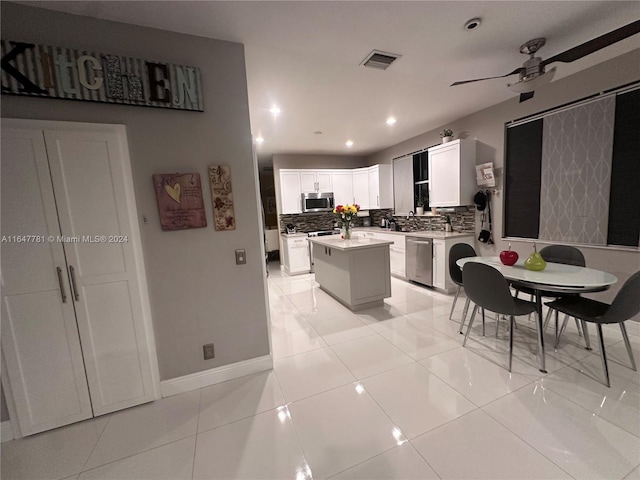 kitchen featuring stainless steel appliances, a center island, ceiling fan, decorative backsplash, and white cabinets