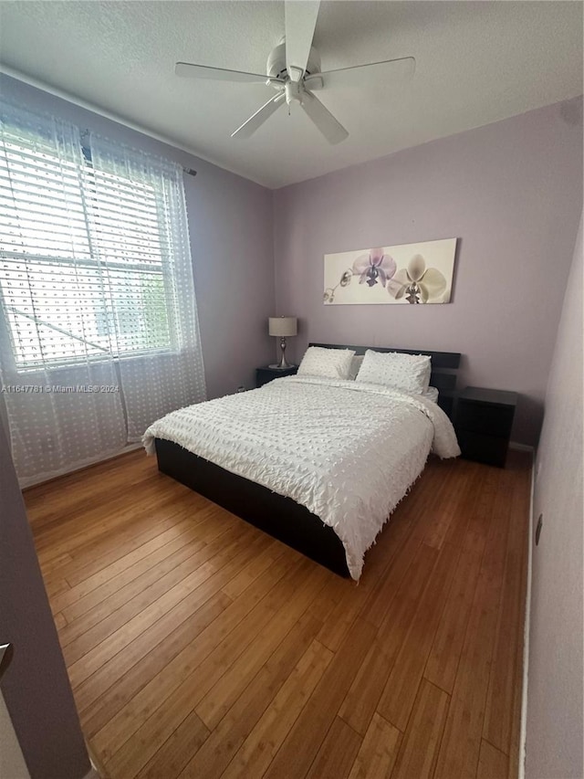 bedroom with a textured ceiling, hardwood / wood-style flooring, and ceiling fan