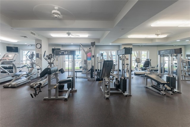 exercise room featuring ceiling fan, a wealth of natural light, and a tray ceiling