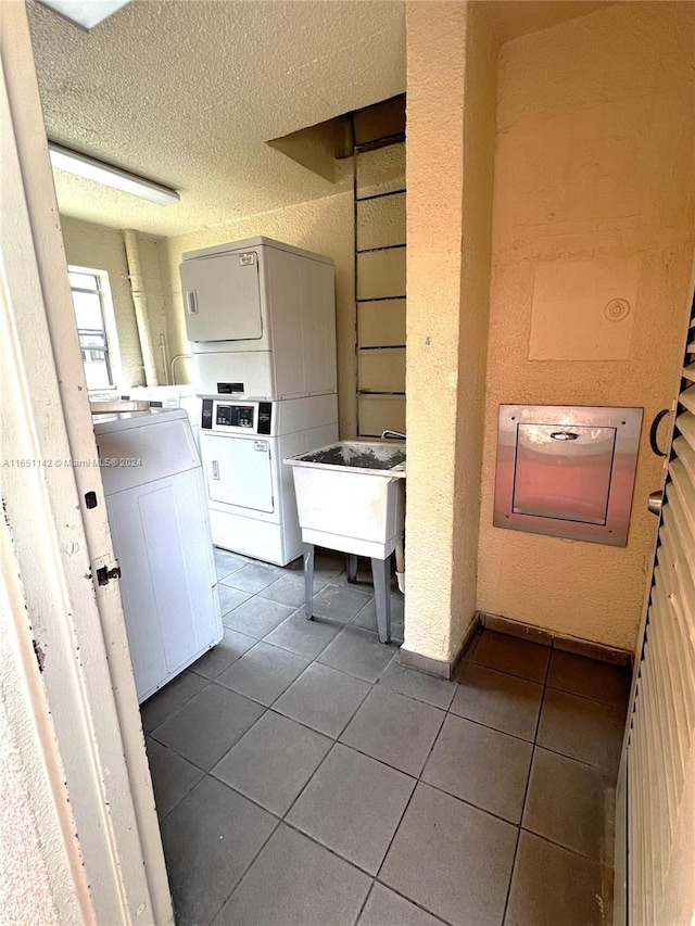 laundry room featuring a textured ceiling, stacked washer / drying machine, dark tile patterned flooring, washer and dryer, and sink