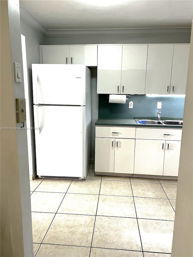 kitchen with white fridge, ornamental molding, light tile patterned floors, sink, and white cabinets