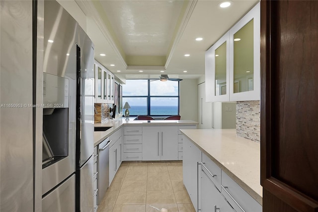 kitchen featuring white cabinetry, appliances with stainless steel finishes, decorative backsplash, a tray ceiling, and a water view