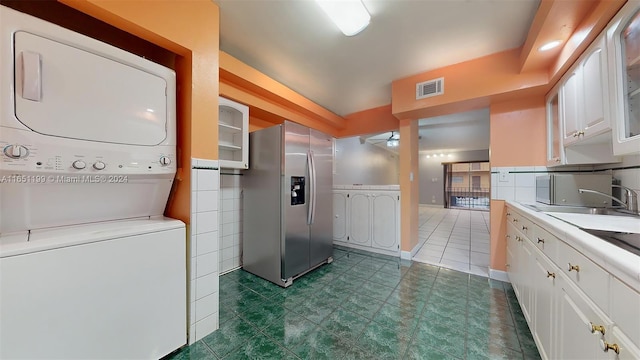 laundry area featuring stacked washer / drying machine, ceiling fan, and dark tile patterned floors