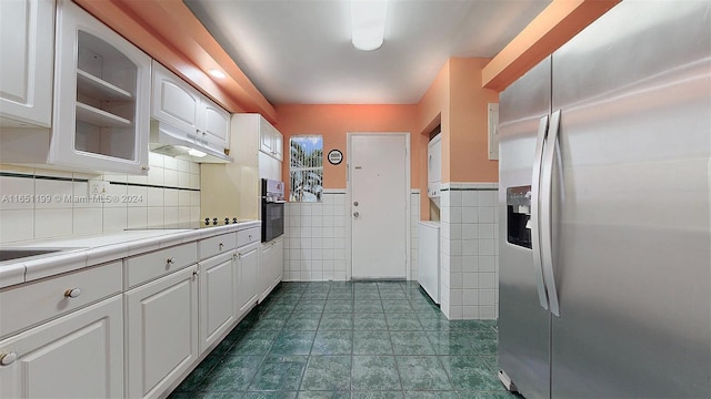 kitchen with dark tile patterned floors, oven, white cabinetry, stainless steel refrigerator with ice dispenser, and tile countertops