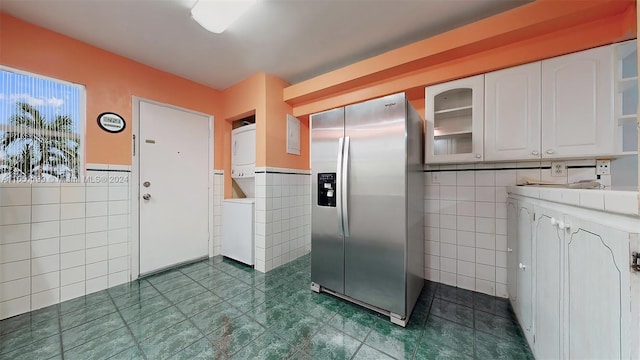 kitchen featuring tile walls, stainless steel fridge, stacked washer / drying machine, and white cabinetry