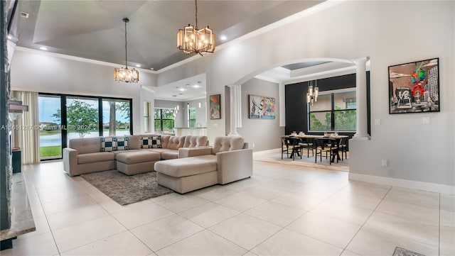 tiled living room with a towering ceiling, a raised ceiling, an inviting chandelier, and ornate columns