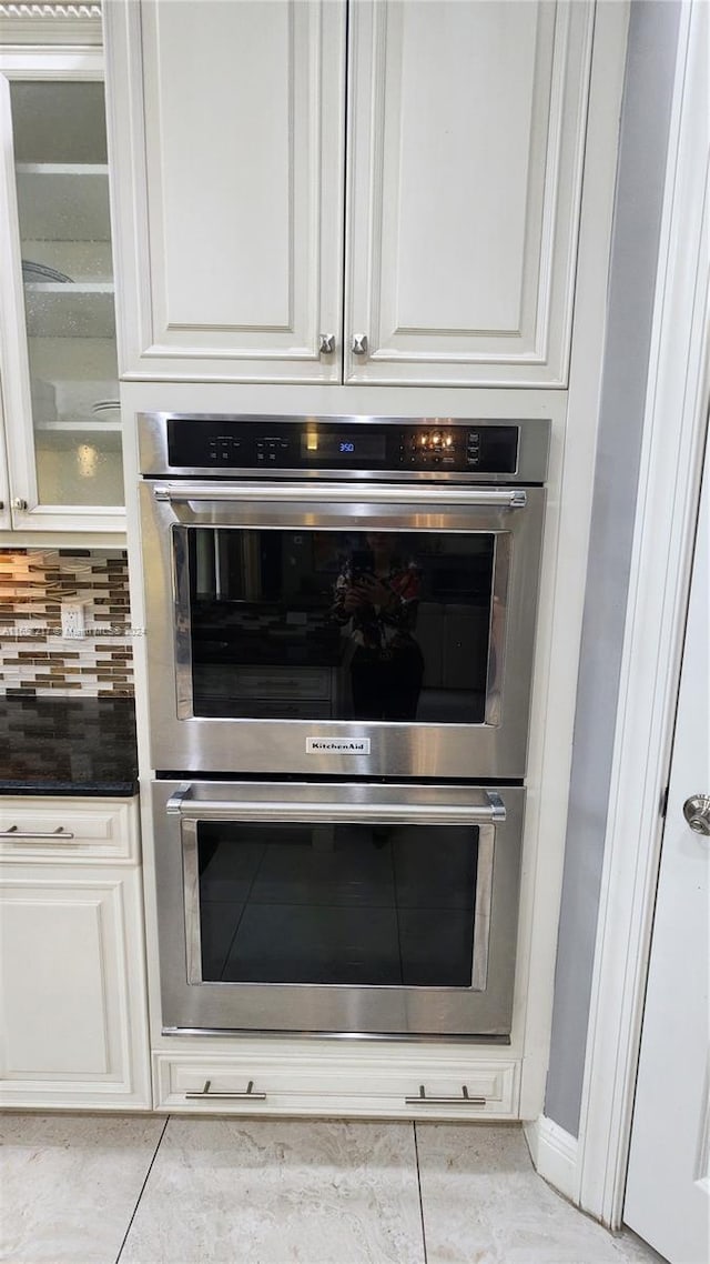 interior details featuring double oven, decorative backsplash, and white cabinetry