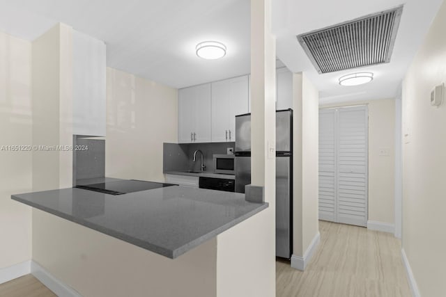 kitchen with stainless steel refrigerator, white cabinetry, kitchen peninsula, black electric cooktop, and light hardwood / wood-style floors