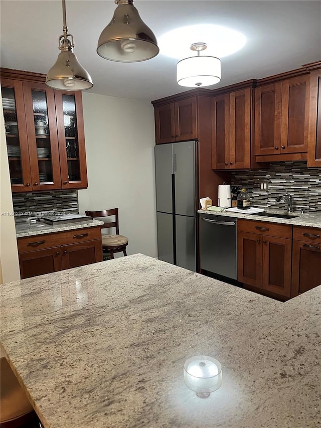 kitchen with appliances with stainless steel finishes, tasteful backsplash, hanging light fixtures, sink, and light stone counters