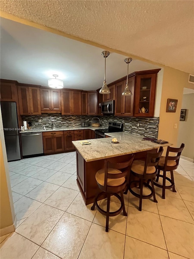 kitchen with tasteful backsplash, appliances with stainless steel finishes, decorative light fixtures, a peninsula, and light stone countertops