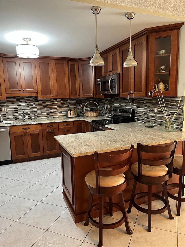 kitchen featuring decorative light fixtures, backsplash, appliances with stainless steel finishes, light stone countertops, and a peninsula