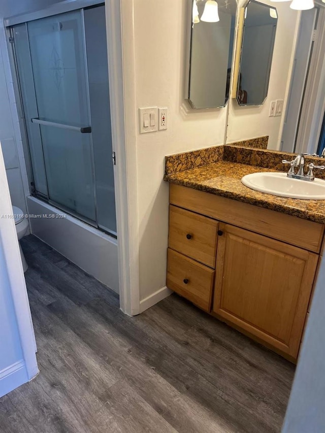 full bathroom with vanity, toilet, hardwood / wood-style flooring, and enclosed tub / shower combo