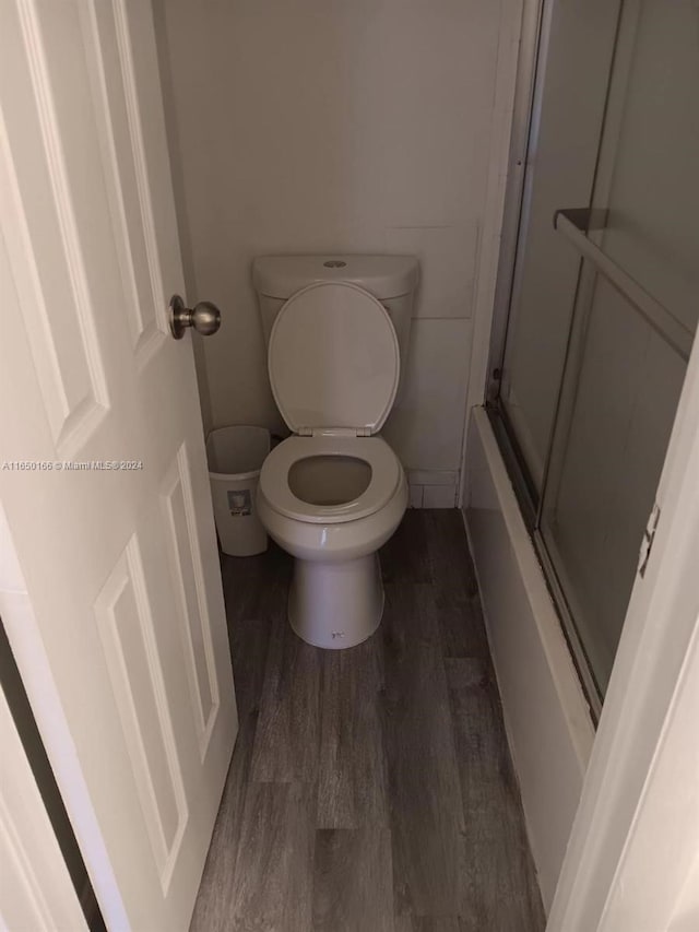 bathroom featuring combined bath / shower with glass door, toilet, and hardwood / wood-style flooring