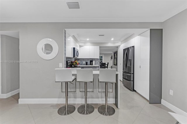 kitchen with a kitchen breakfast bar, kitchen peninsula, white cabinetry, ornamental molding, and stainless steel appliances