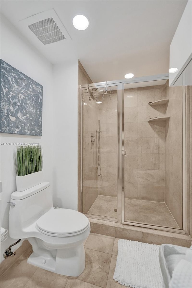 bathroom with tile patterned flooring, toilet, and a shower with door