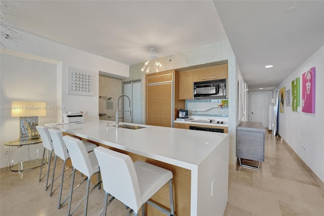 kitchen featuring a breakfast bar area, a center island with sink, black appliances, backsplash, and sink