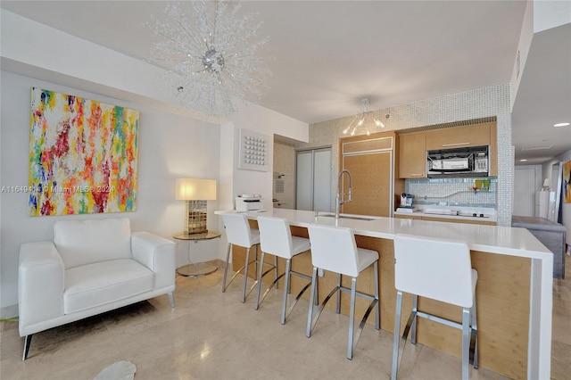 kitchen with white cooktop, tasteful backsplash, a kitchen breakfast bar, an inviting chandelier, and sink