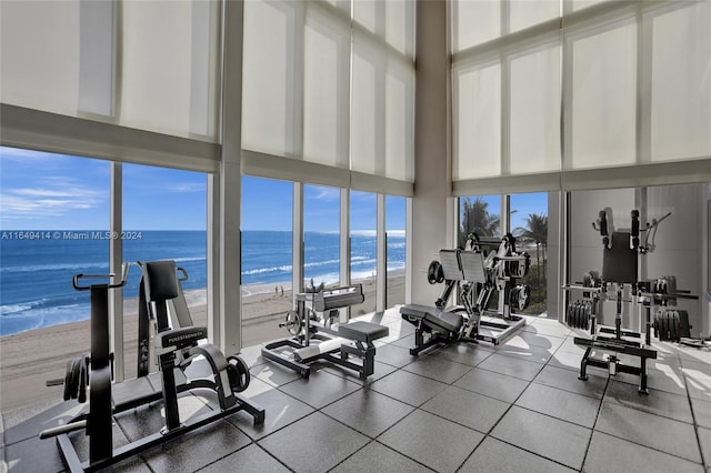 workout area featuring a view of the beach, a towering ceiling, a wall of windows, and a water view