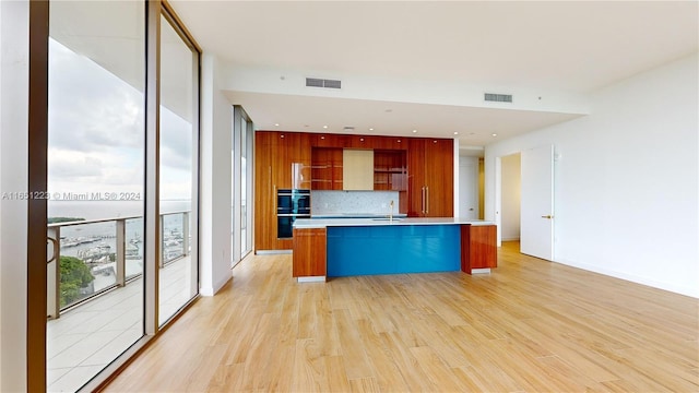 kitchen with a kitchen island with sink, tasteful backsplash, sink, and light hardwood / wood-style floors