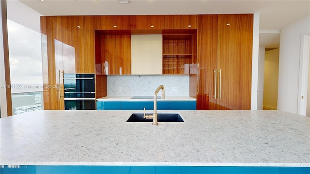 kitchen with black double oven, light stone counters, tasteful backsplash, and sink