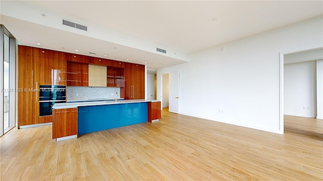 kitchen with light hardwood / wood-style flooring, an island with sink, sink, decorative backsplash, and double oven