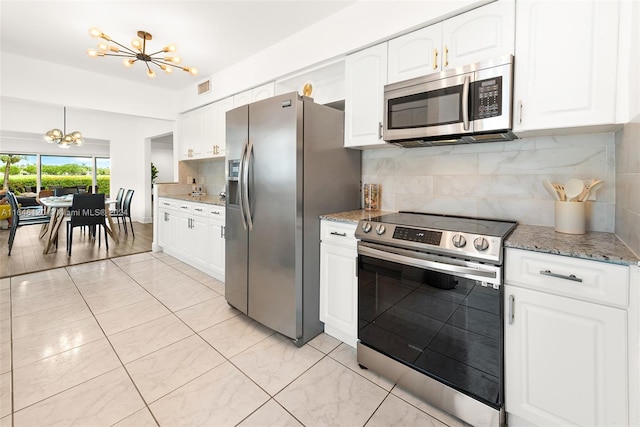 kitchen featuring backsplash, appliances with stainless steel finishes, white cabinetry, a chandelier, and light stone counters