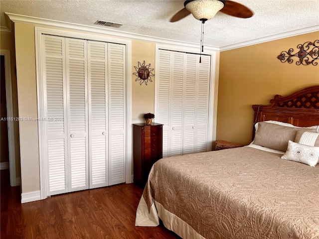 bedroom with two closets, dark wood-type flooring, visible vents, ornamental molding, and a textured ceiling