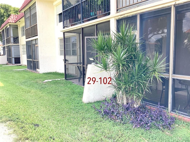 view of exterior entry featuring a balcony and a lawn