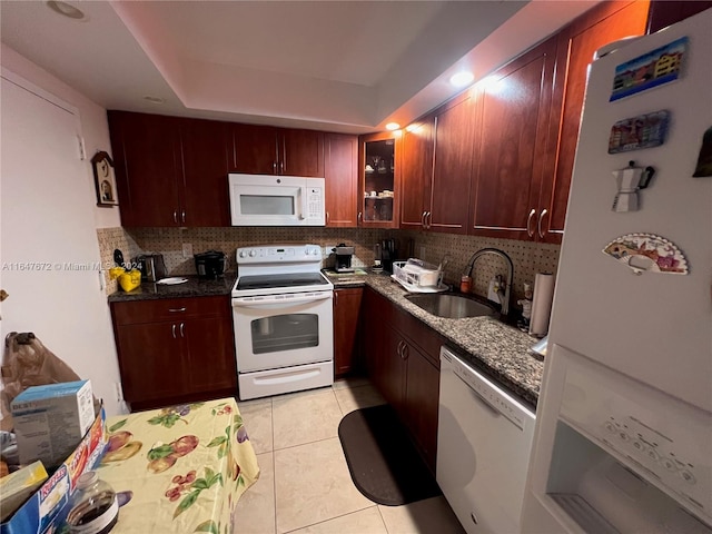 kitchen with dark stone counters, white appliances, light tile patterned floors, and sink